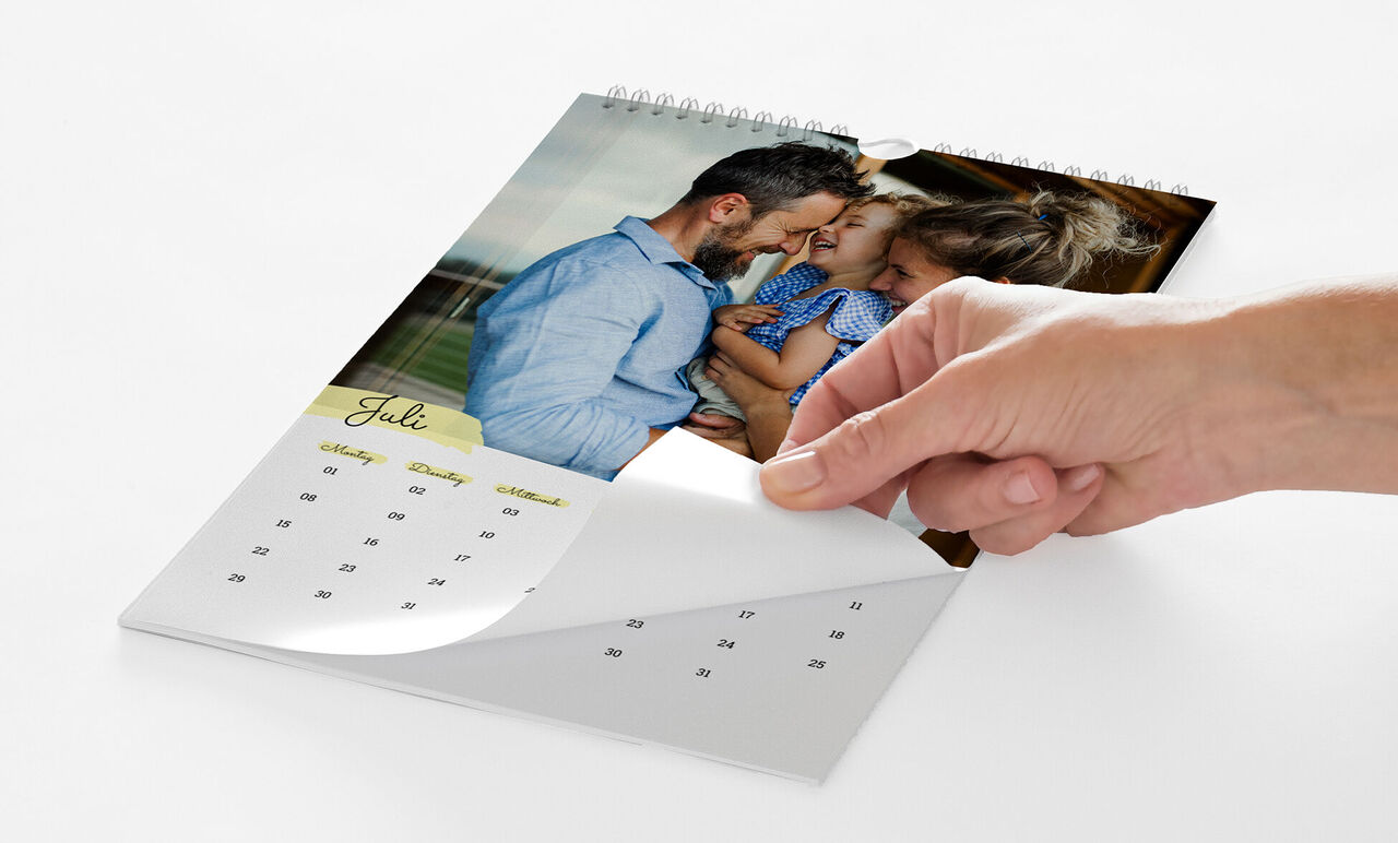 Eine Hand blättert von einem Kalenderblatt mit einem Foto von Eltern mit ihrem Kind zum nächsten Monat.
