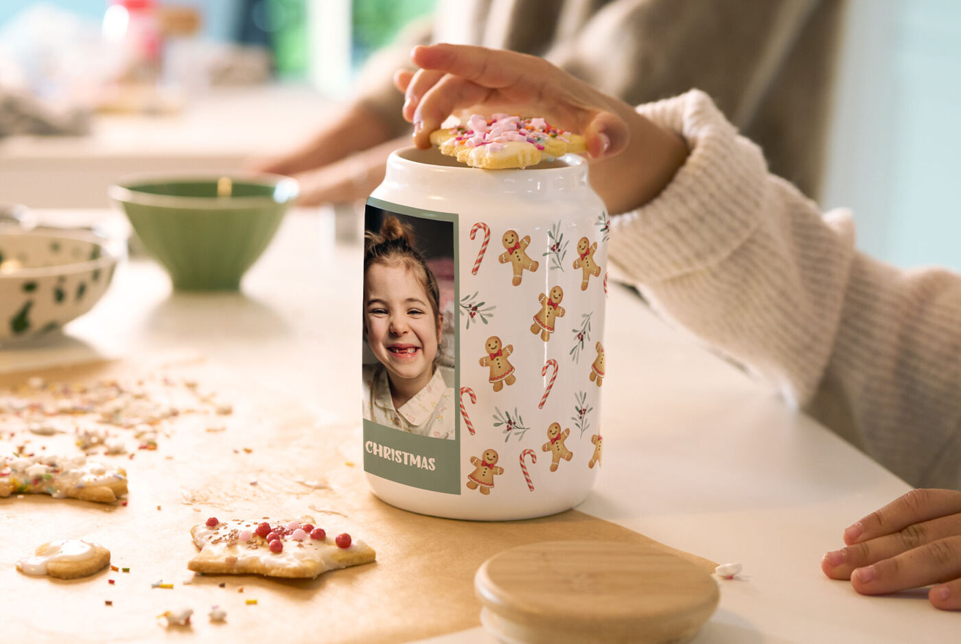 Weiße Keramikdose mit Kinderfoto und Weihnachtsdesign steht auf einem Tisch und wird von einer Kinderhand mit Keksen befüllt