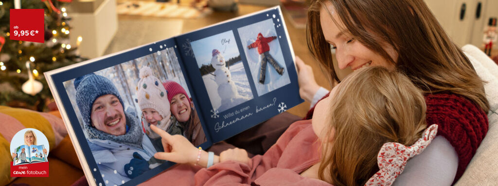 Eine Mutter sitzt mit ihrer Tocher auf einem Sofa und blättert in einem aufgeschlagenen CEWE FOTOBUCH mit Winterfotos von der Familie