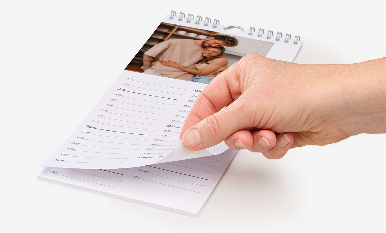 Eine Hand blättert von einem Kalenderblatt mit einem Foto eines Paares zum nächsten Monat.