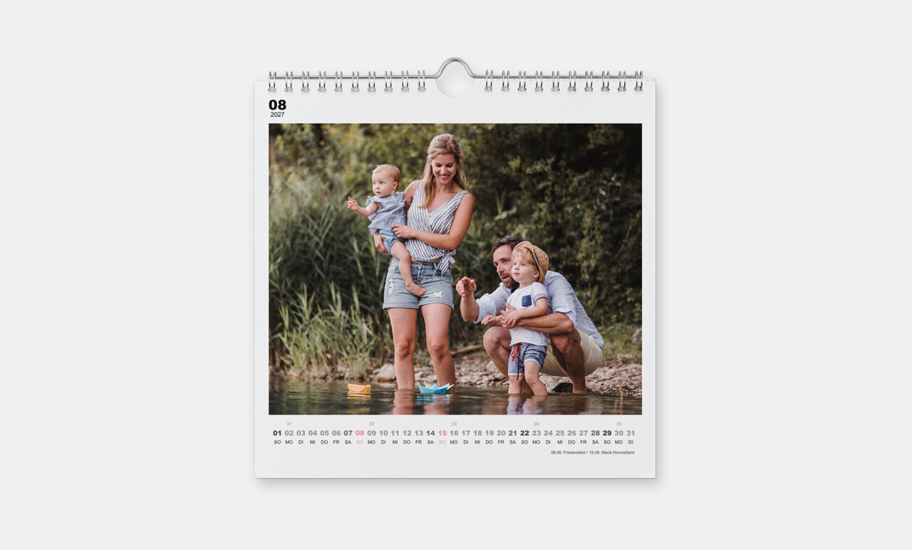 Quadratischer Kalender mit Spiralbindung und einem einfachen, weißen Design und einem Foto von einer Familie am Wasser.