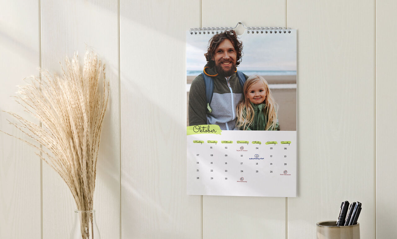 Kalender im Hochformat mit Spiralbindung, Design mit Farbakzenten und Foto von Vater und Tochter, hängt an der Wand.