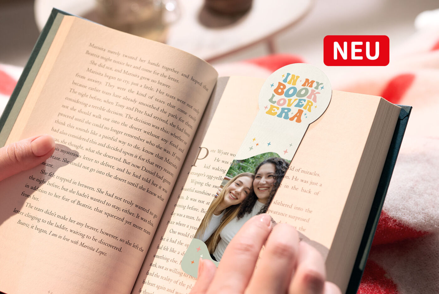 Ein Lesezeichen mit abgerundetem Kopfteil, Foto von zwei Freundinnen und Schriftzug "in my book lover era" wird in ein Buch gesteckt