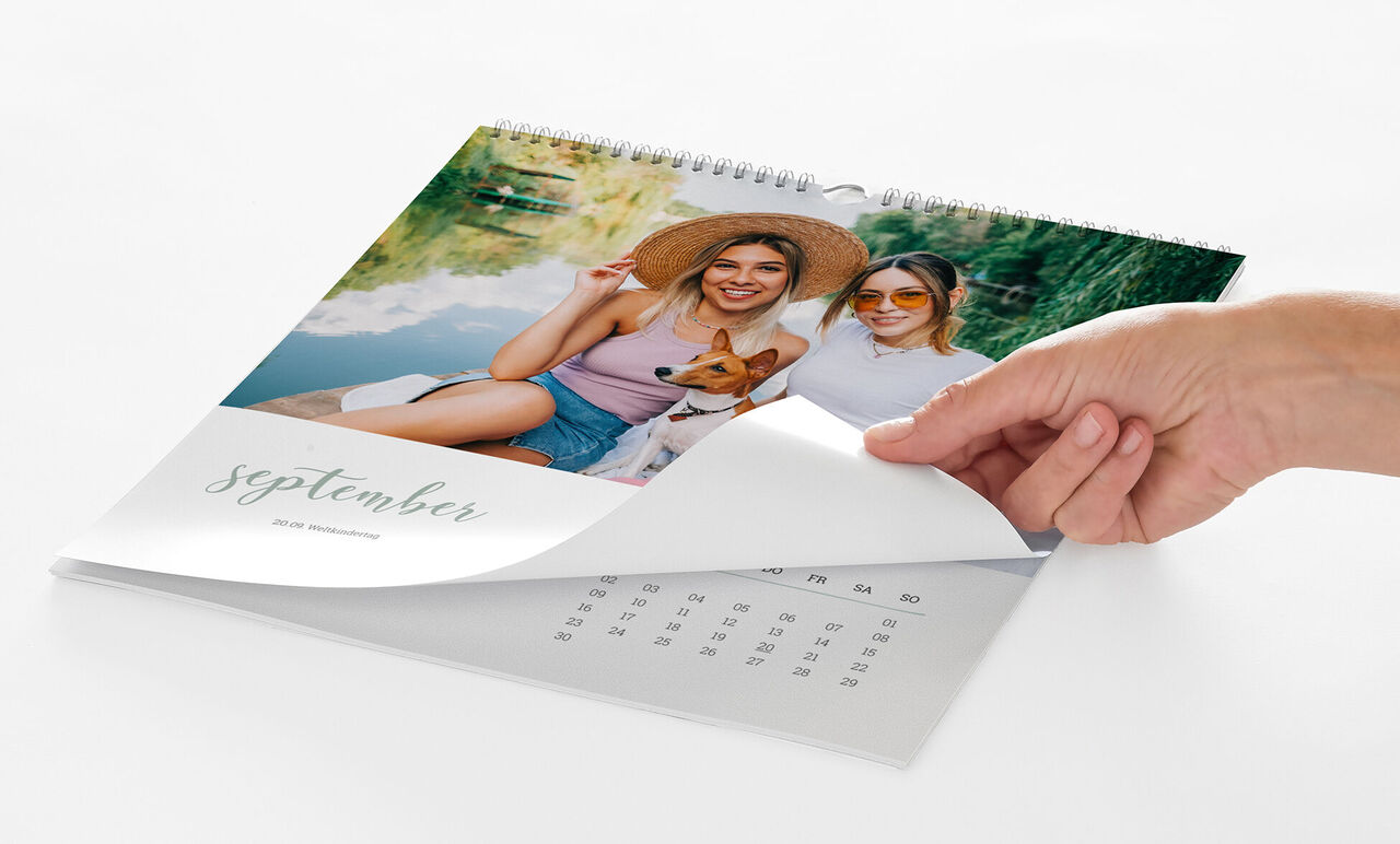 Eine Hand blättert von einem Kalenderblatt mit einem Foto von zwei jungen Frauen mit Hund zum nächsten Monat.