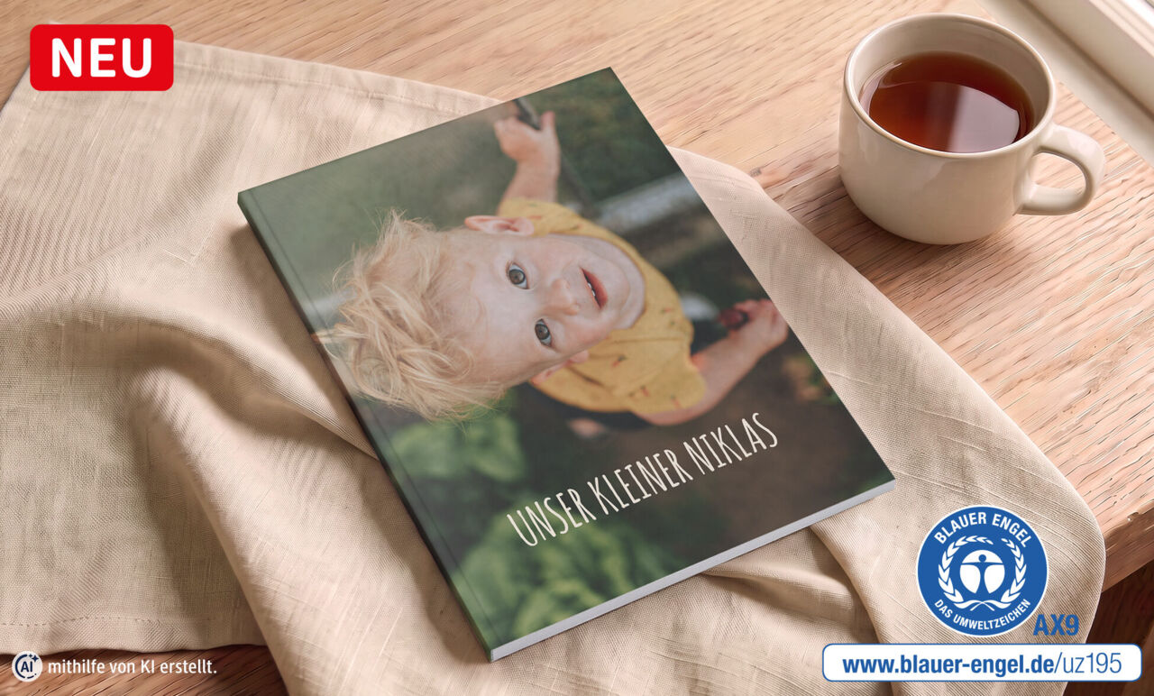 Fotobuch mit einem Bild von einem Jungen liegt auf einem Tisch. Daneben ist der Blaue Engel abgebildet.