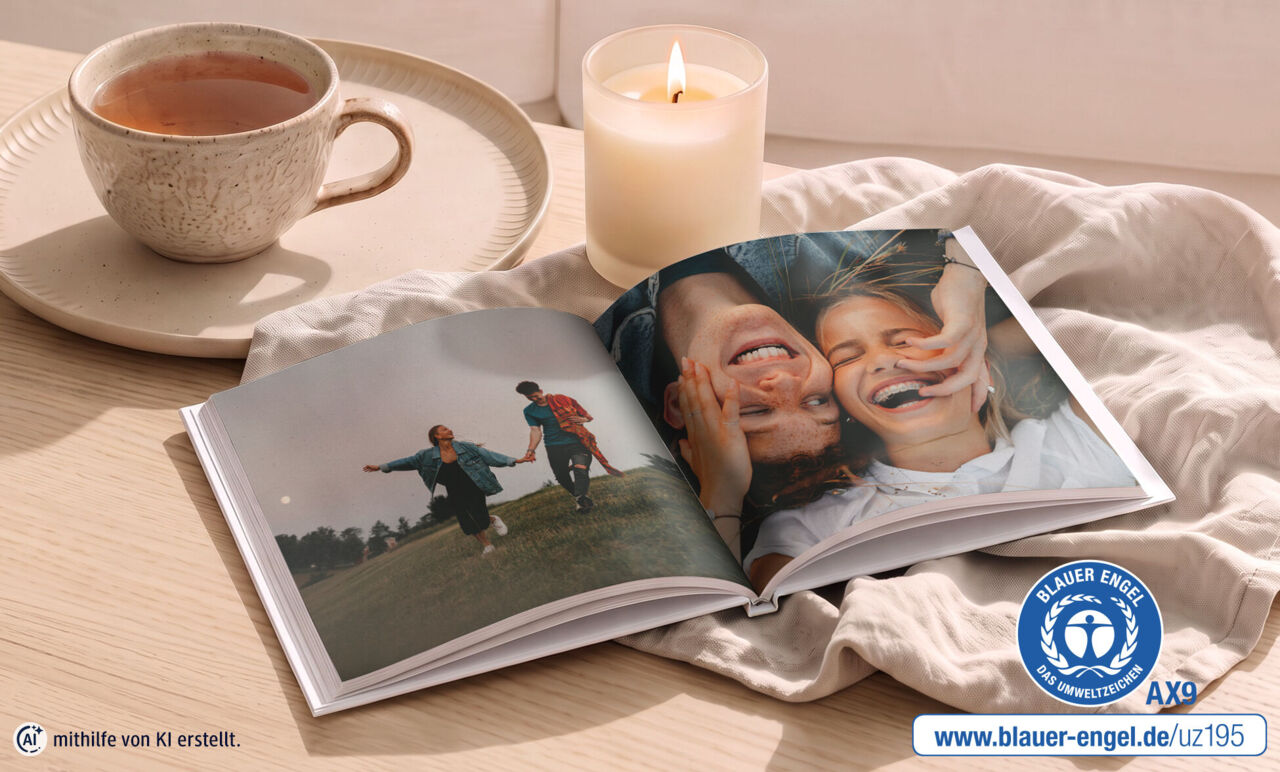 Geöffnetes Fotobuch mit Paarbildern liegt auf einem Tisch. Daneben ist der Blaue Engel abgebildet.