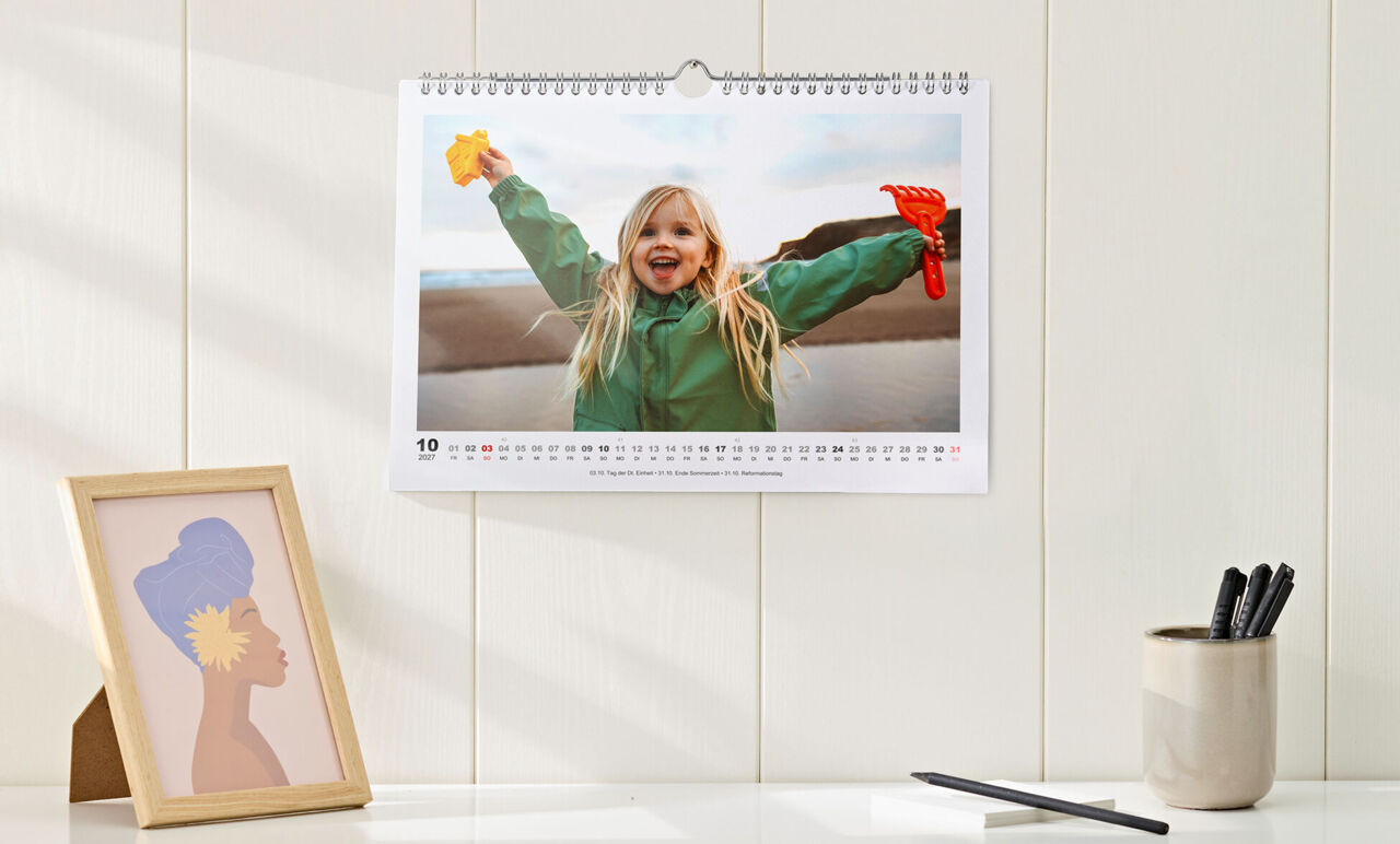 Kalender im Querformat mit Spiralbindung und einfachem, weißem Design, mit Foto von einem Mädchen, hängt über Sideboard