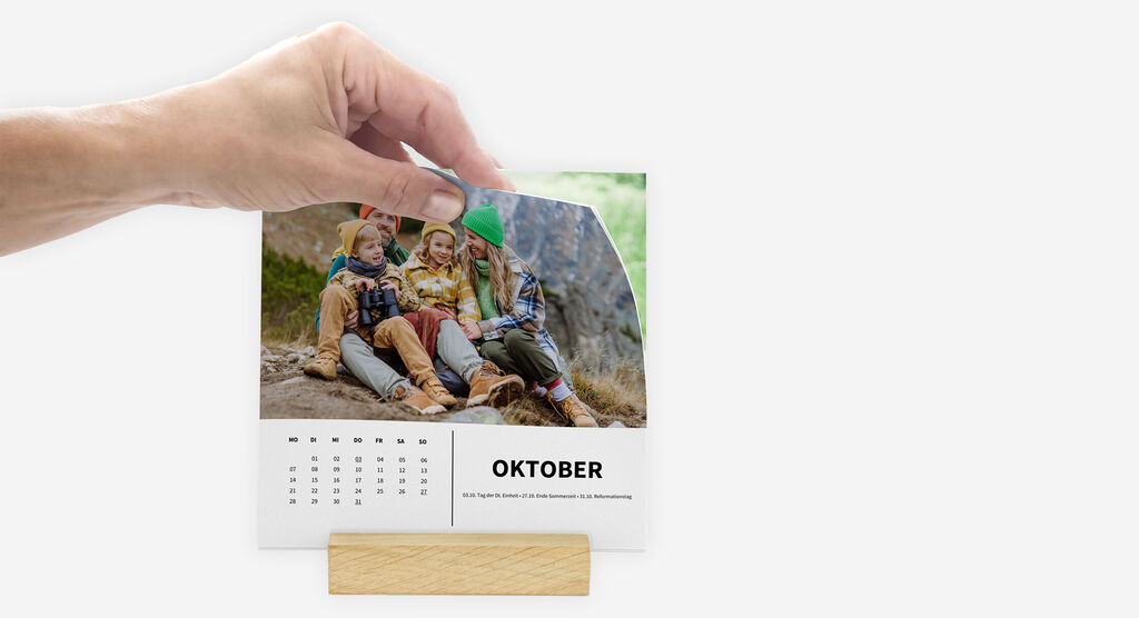 Eine Hand zeigt durch Auffächern der Kalenderblätter, dass diese frei im Holzstandfuß stehen und nicht gebunden sind.